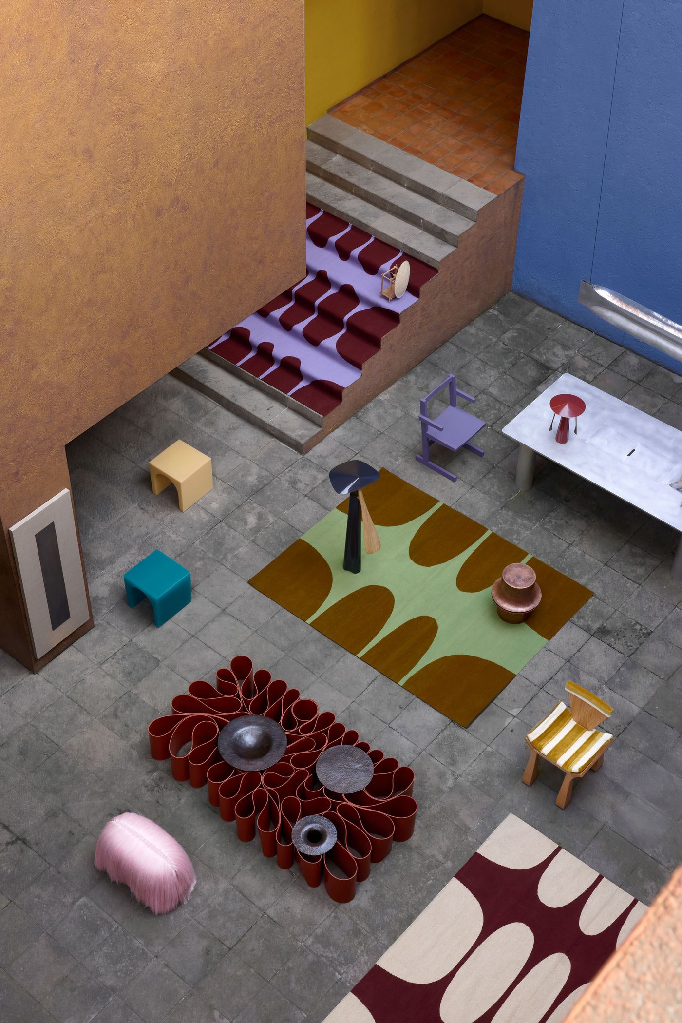 An artistic courtyard features colorful furniture, vibrant rugs, and a variety of textures, showcasing modern design elements.