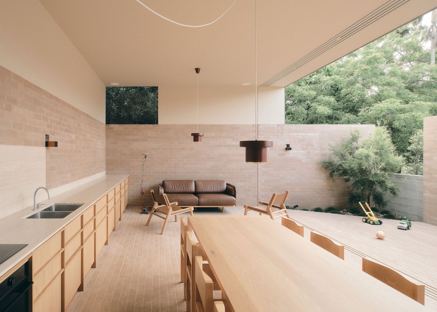 A modern, minimalist interior featuring a wooden dining table, a brown leather sofa, and greenery visible through large windows. A modern, minimalist interior featuring a wooden dining table, a brown leather sofa, and greenery visible through large windows.