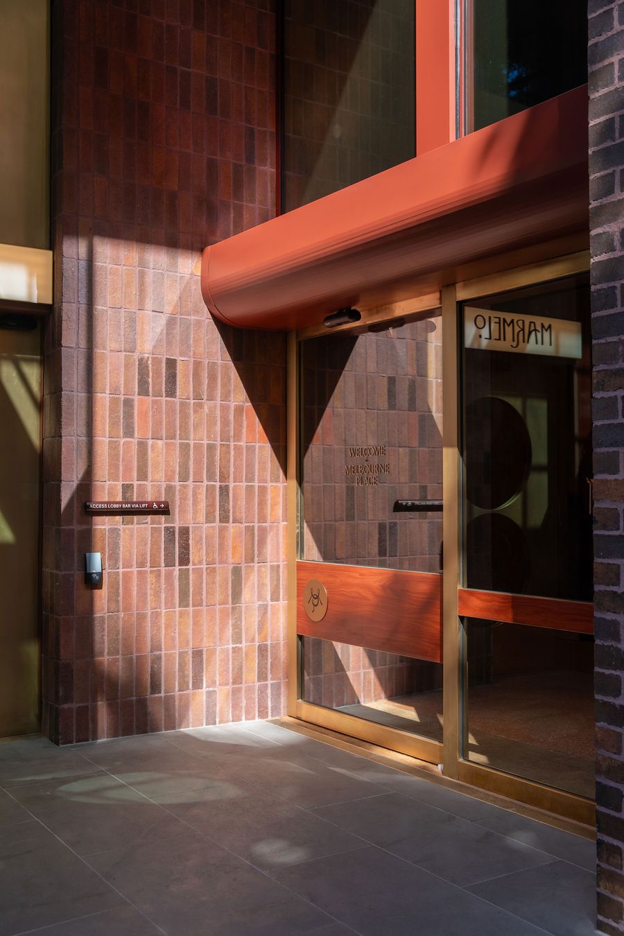 Entrance of a modern building with textured brick walls, a wooden door, and a welcoming sign, illuminated by soft sunlight. Entrance of a modern building with textured brick walls, a wooden door, and a welcoming sign, illuminated by soft sunlight.