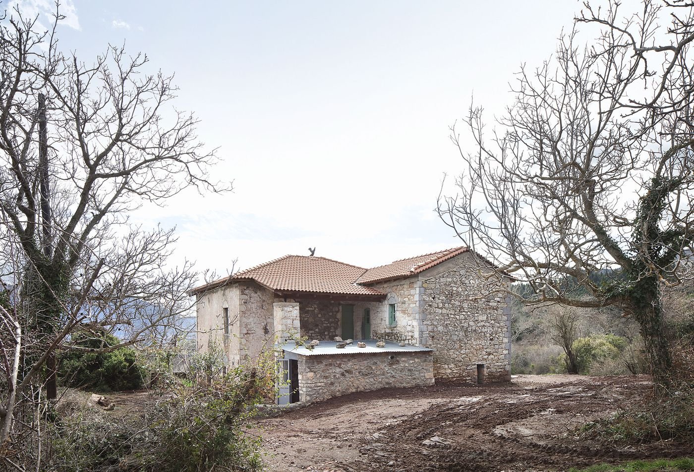 Ancient stone walls frame a Mediterranean restoration where weathered limestone meets contemporary terracotta roofing. The rustic landscape setting showcases the building's organic integration with its natural surroundings, emphasizing authenticity through material preservation.