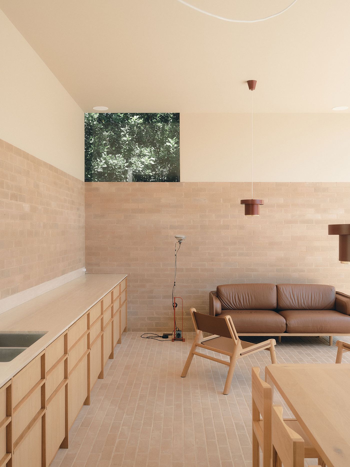 A minimalist interior featuring a brown leather sofa, light wood furniture, and a brick wall, with a glimpse of greenery through a window. A minimalist interior featuring a brown leather sofa, light wood furniture, and a brick wall, with a glimpse of greenery through a window.