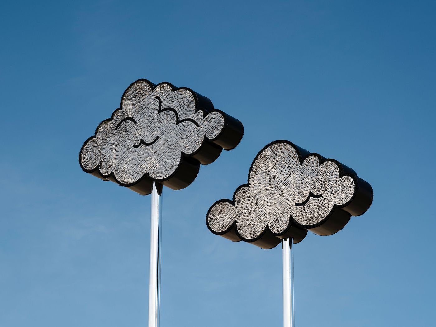 Two large, stylized metal cloud sculptures with intricate designs against a clear blue sky. Two large, stylized metal cloud sculptures with intricate designs against a clear blue sky.