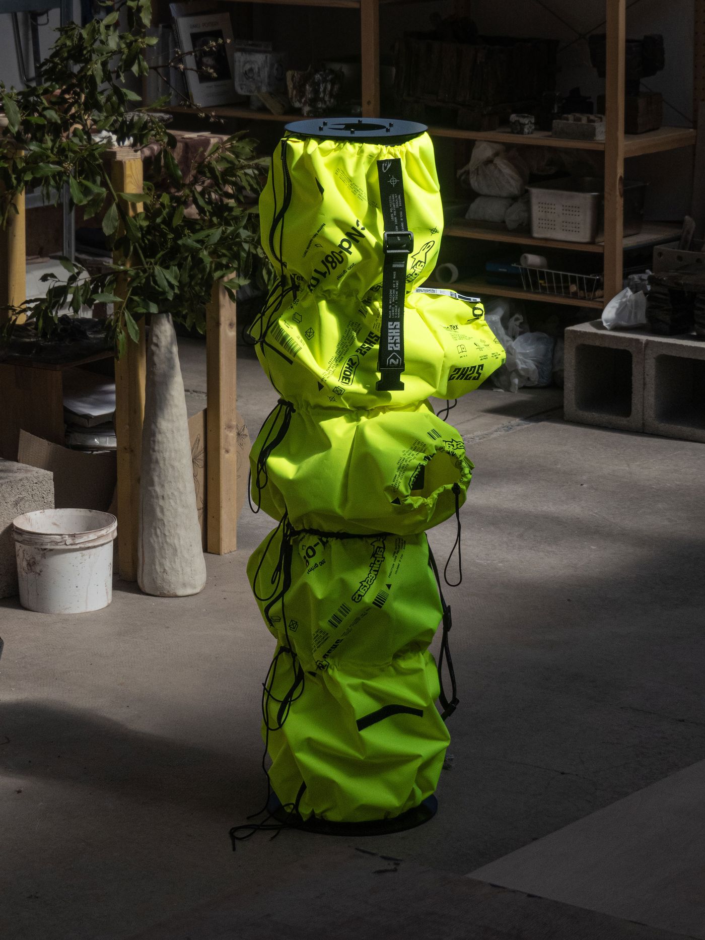 A stack of bright yellow, flexible containers with black straps, set against a cluttered background in a sunlit indoor space.