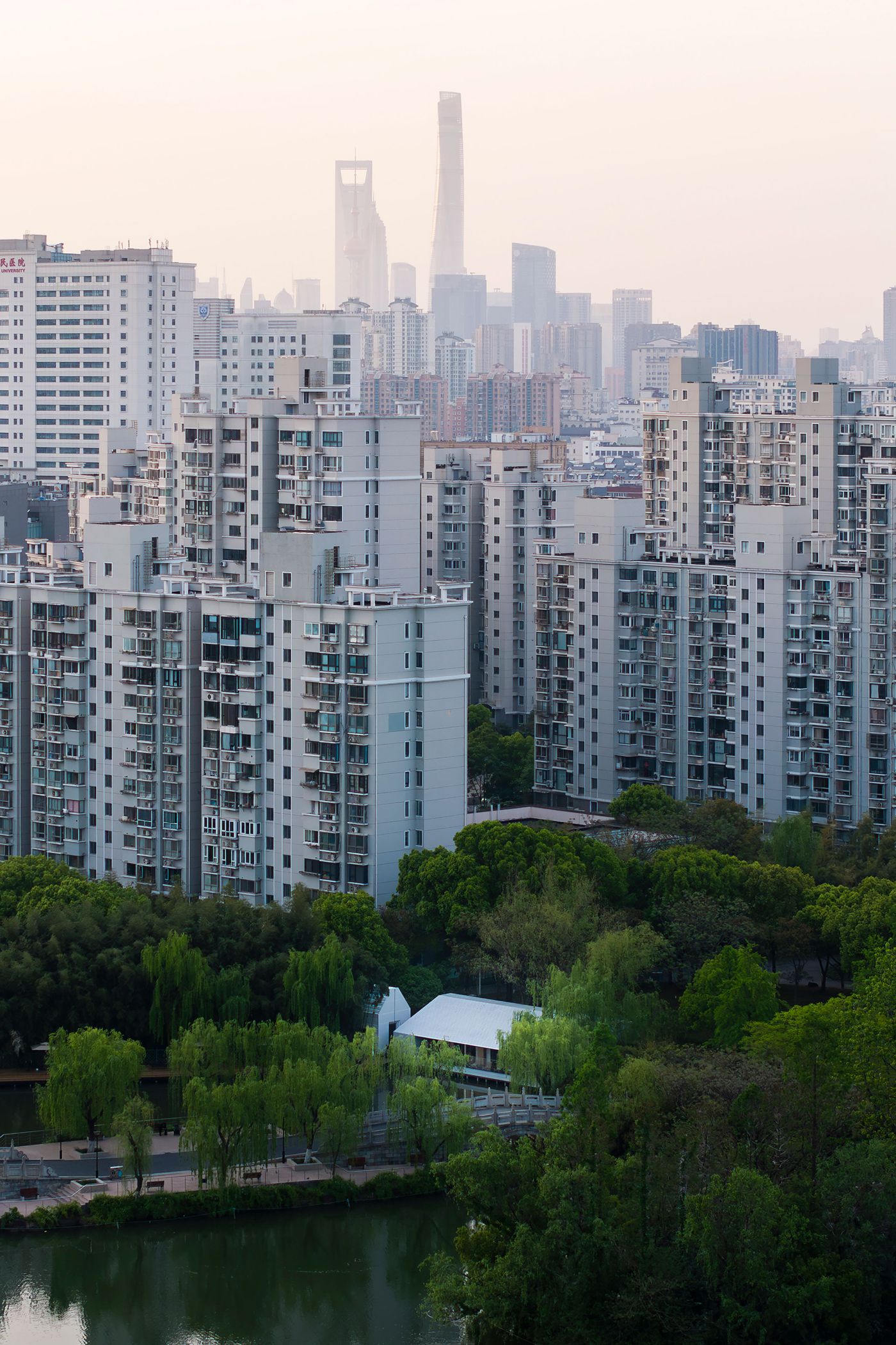 A distant, elevated perspective reveals Wutopia Lab's Lake House in Shanghai, a subtle presence of minimalist design amidst a dense urban backdrop. The pristine white, gabled structure is framed by lush green trees and a tranquil lake, sharply contrasting with the towering, grey residential buildings of the city skyline, which recede into a hazy horizon, emphasizing the dwelling's secluded, serene character. A distant, elevated perspective reveals Wutopia Lab's Lake House in Shanghai, a subtle presence of minimalist design amidst a dense urban backdrop. The pristine white, gabled structure is framed by lush green trees and a tranquil lake, sharply contrasting with the towering, grey residential buildings of the city skyline, which recede into a hazy horizon, emphasizing the dwelling's secluded, serene character.