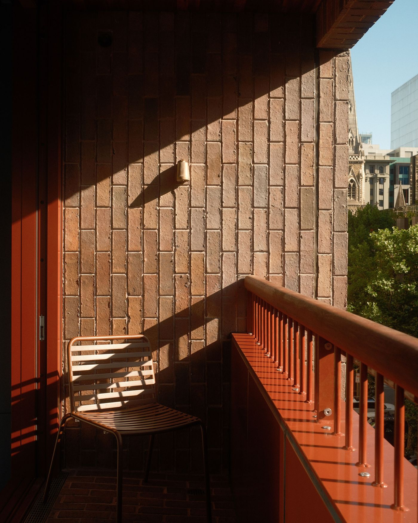 A sunlit balcony features a metal chair against a brick wall, with shadows creating a warm, inviting atmosphere.