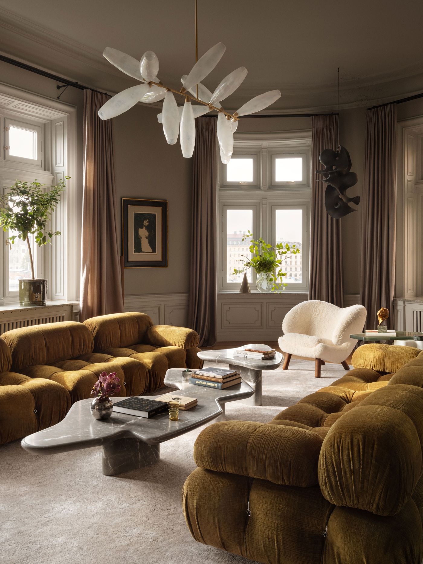 A stylish living room featuring mustard velvet sofas, a sculptural marble coffee table, and a unique chandelier with glass accents. A stylish living room featuring mustard velvet sofas, a sculptural marble coffee table, and a unique chandelier with glass accents.