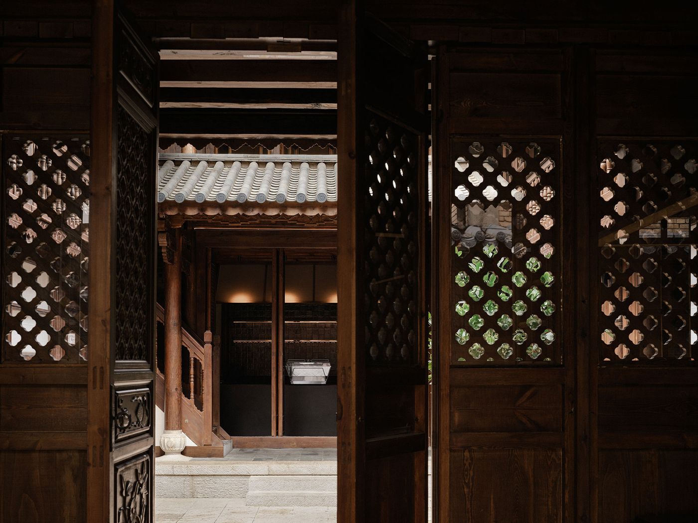 A view through ornate wooden doors reveals a serene courtyard with traditional architecture and lush greenery. A view through ornate wooden doors reveals a serene courtyard with traditional architecture and lush greenery.