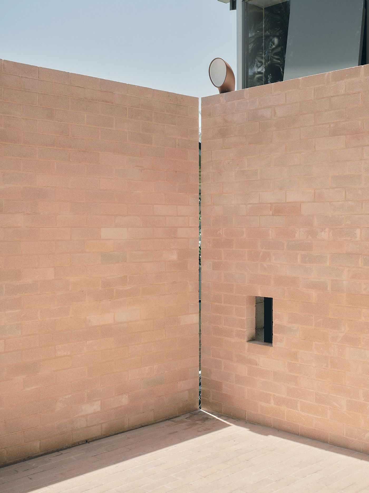 Two intersecting light-colored brick walls create an open corner, featuring a small window and a circular speaker on top. Two intersecting light-colored brick walls create an open corner, featuring a small window and a circular speaker on top.
