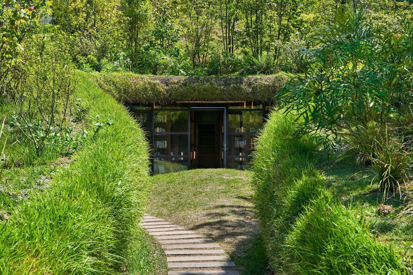 A modern, eco-friendly building with a grassy roof surrounded by lush greenery and a wooden path leading to its glass entrance. A modern, eco-friendly building with a grassy roof surrounded by lush greenery and a wooden path leading to its glass entrance.