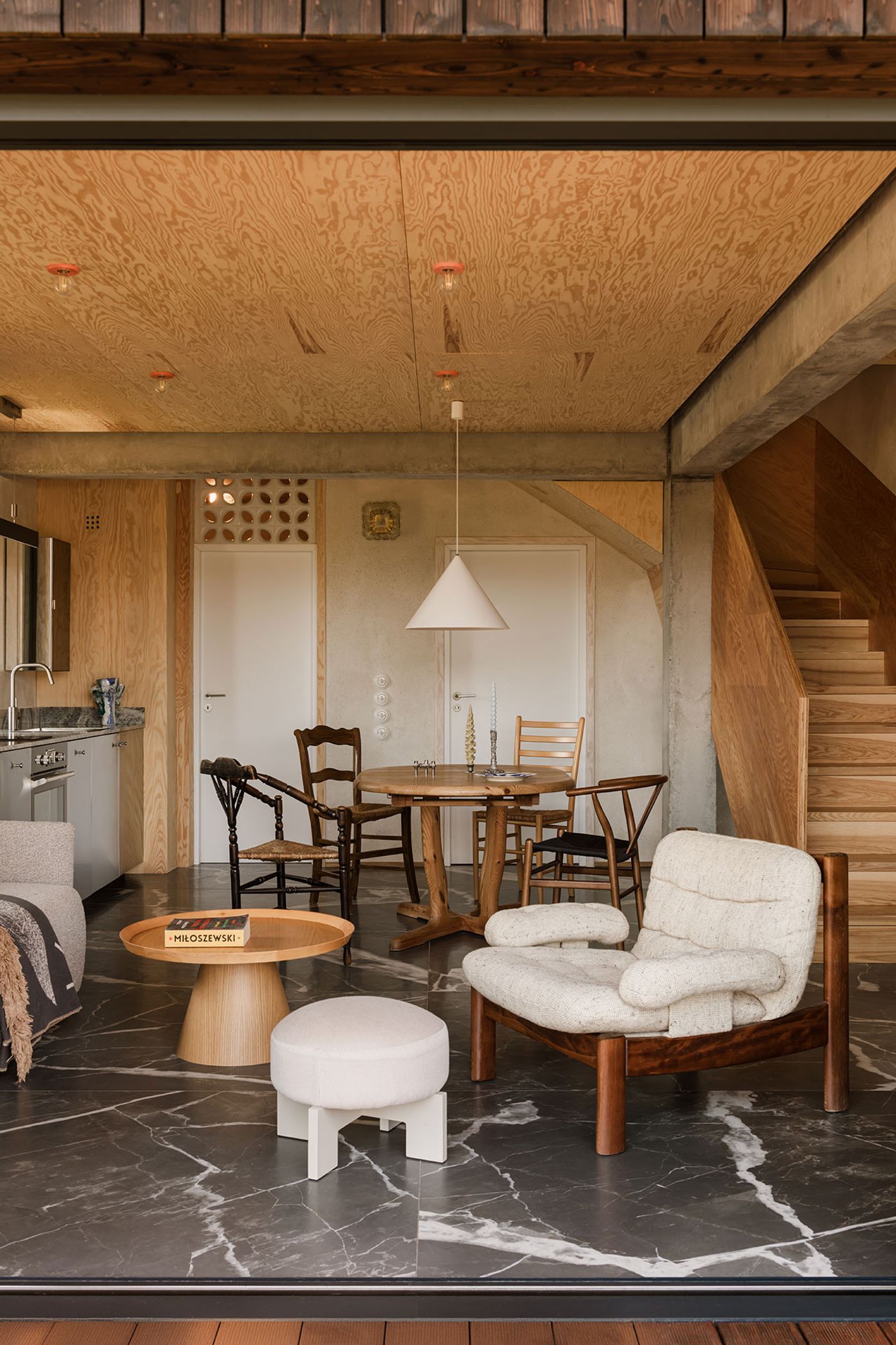 A cozy, modern living space featuring a mix of wooden furniture, stylish chairs, and a marble floor, with an inviting atmosphere. A cozy, modern living space featuring a mix of wooden furniture, stylish chairs, and a marble floor, with an inviting atmosphere.