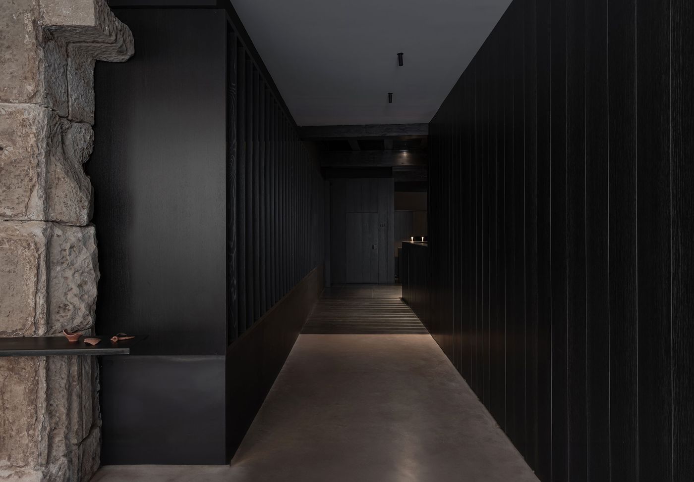Dimly lit corridor showcasing a blend of textured stone and sleek black wood paneling, evoking a modern yet rustic aesthetic. Dimly lit corridor showcasing a blend of textured stone and sleek black wood paneling, evoking a modern yet rustic aesthetic.