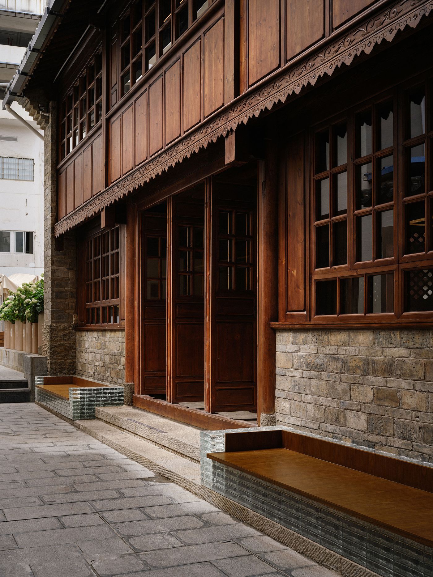 A wooden facade with intricate carvings and large glass windows, flanked by stone walls and a sleek, modern seating area. A wooden facade with intricate carvings and large glass windows, flanked by stone walls and a sleek, modern seating area.