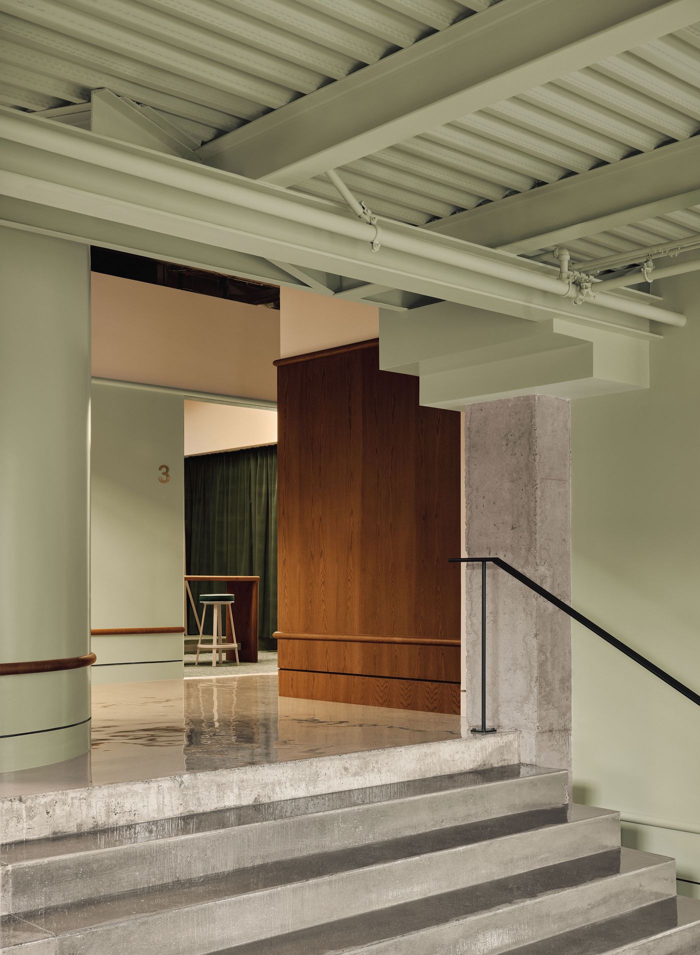 A modern interior featuring concrete stairs, green walls, and wooden accents, leading to a cozy seating area.