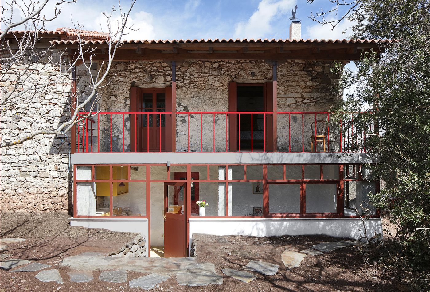 Traditional stone construction meets contemporary living through expansive glazed openings framed in warm coral steel. The ground-level intervention creates seamless indoor-outdoor flow while maintaining the building's historical upper level, showcasing thoughtful restoration philosophy.