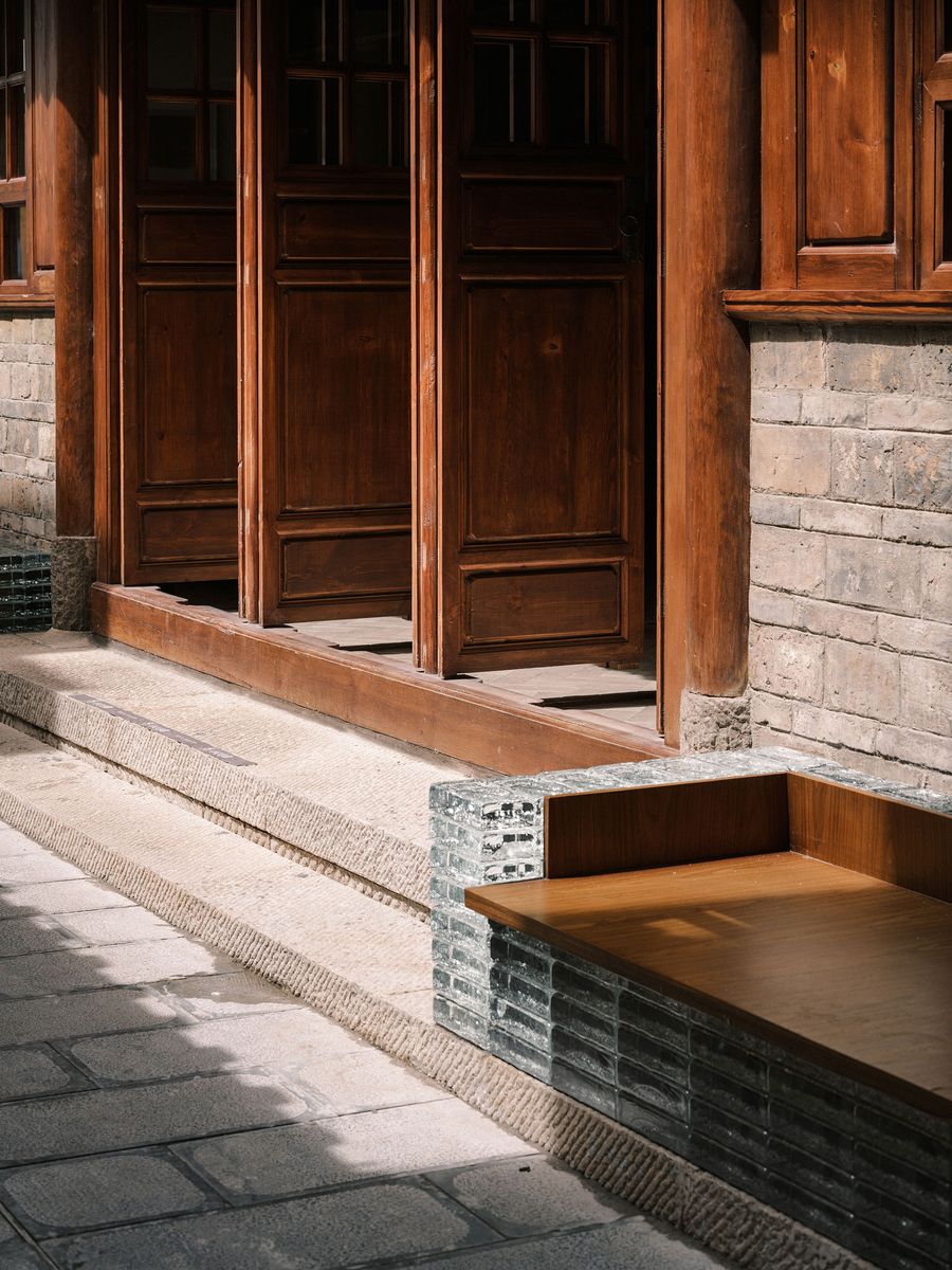 Close-up of a wooden doorway with three panels, leading to a stone step and a minimalist, rectangular wooden platform beside it. Close-up of a wooden doorway with three panels, leading to a stone step and a minimalist, rectangular wooden platform beside it.