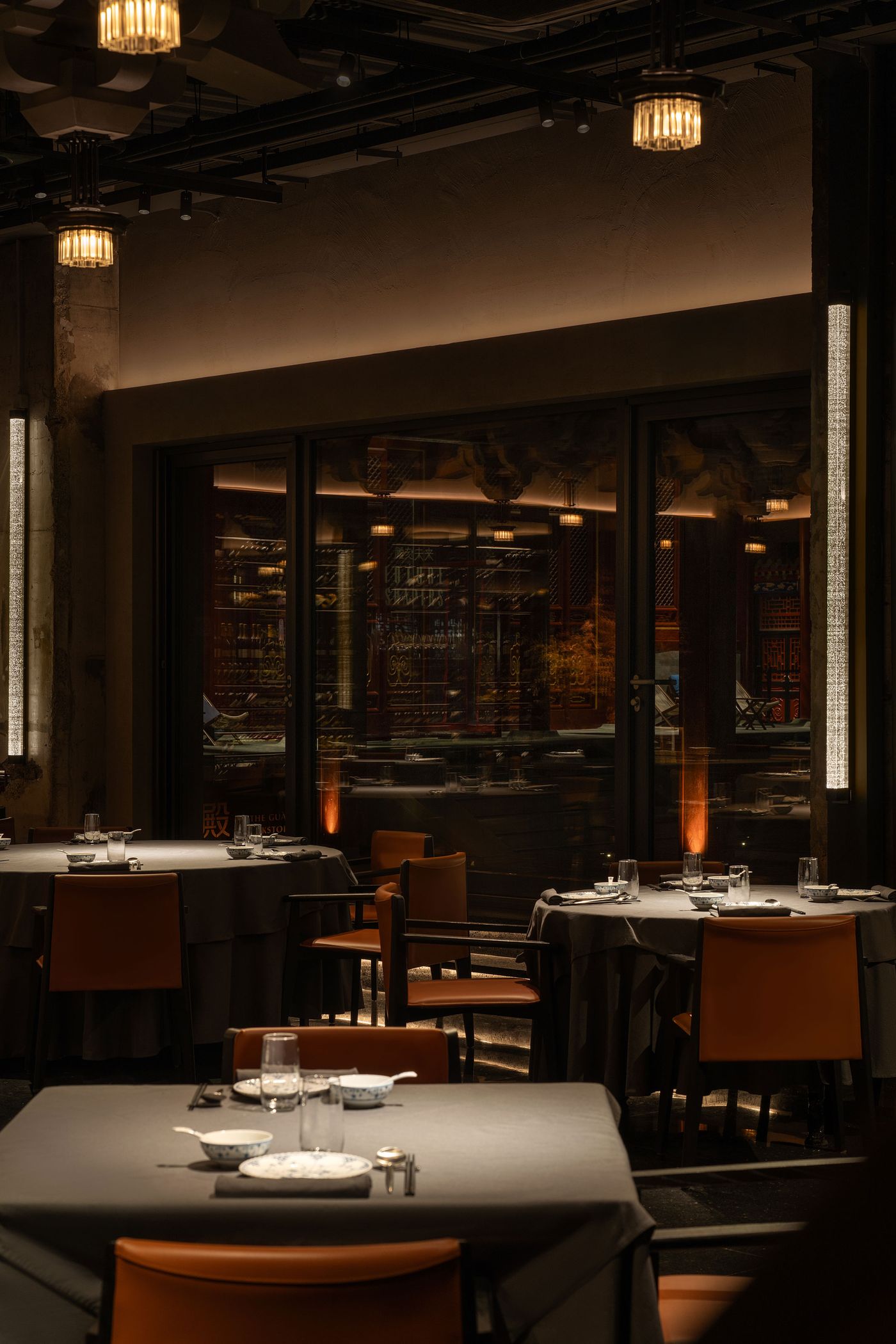 A dimly lit restaurant interior featuring elegantly set tables with gray linens and orange chairs, reflecting a cozy ambiance. A dimly lit restaurant interior featuring elegantly set tables with gray linens and orange chairs, reflecting a cozy ambiance.