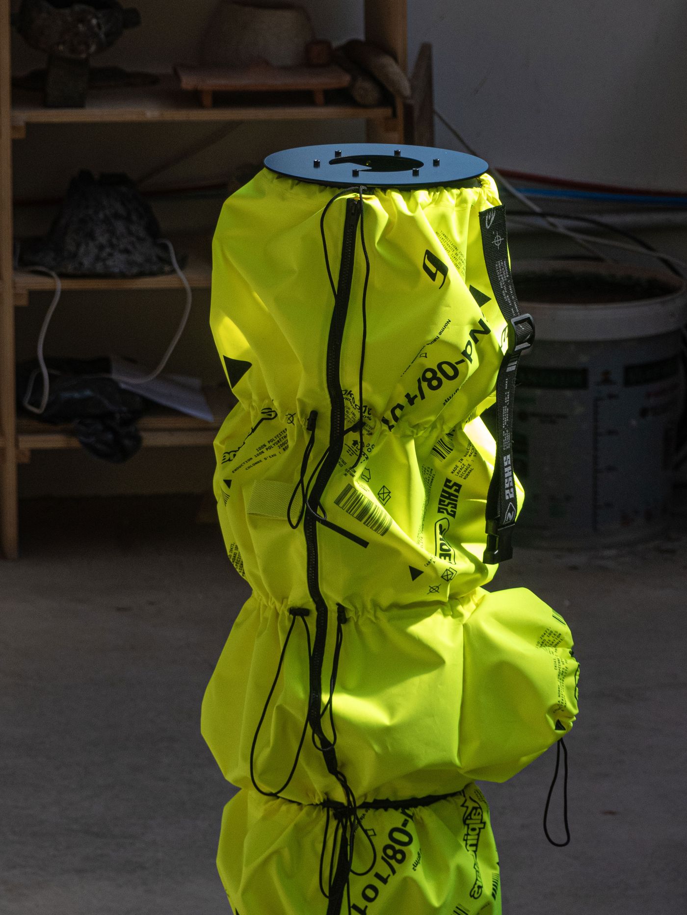 A bright yellow cylindrical object with black markings and a top plate, positioned in a workshop with various tools in the background.