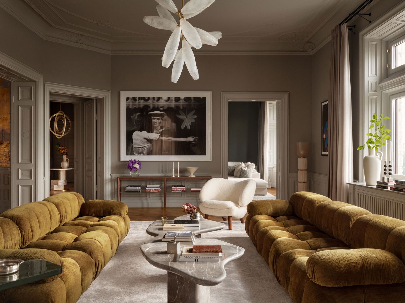 A stylish living room features olive green velvet sofas, a marble coffee table, and elegant decor, illuminated by a unique chandelier. A stylish living room features olive green velvet sofas, a marble coffee table, and elegant decor, illuminated by a unique chandelier.