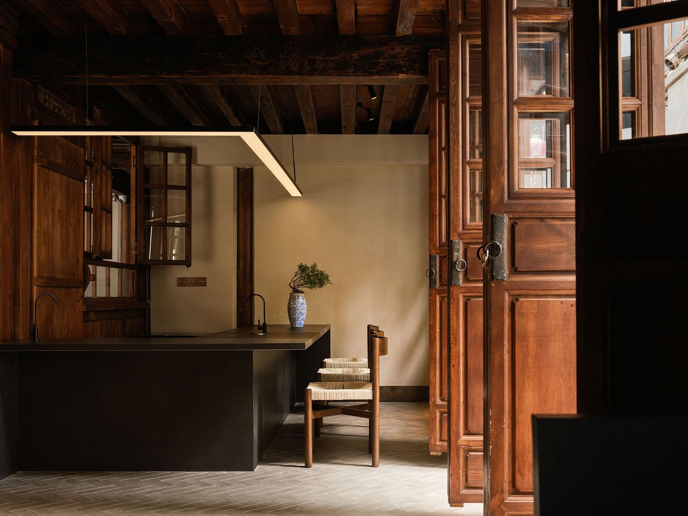 A modern kitchen with a sleek black island, wooden cabinets, and a decorative vase, framed by open wooden doors. A modern kitchen with a sleek black island, wooden cabinets, and a decorative vase, framed by open wooden doors.