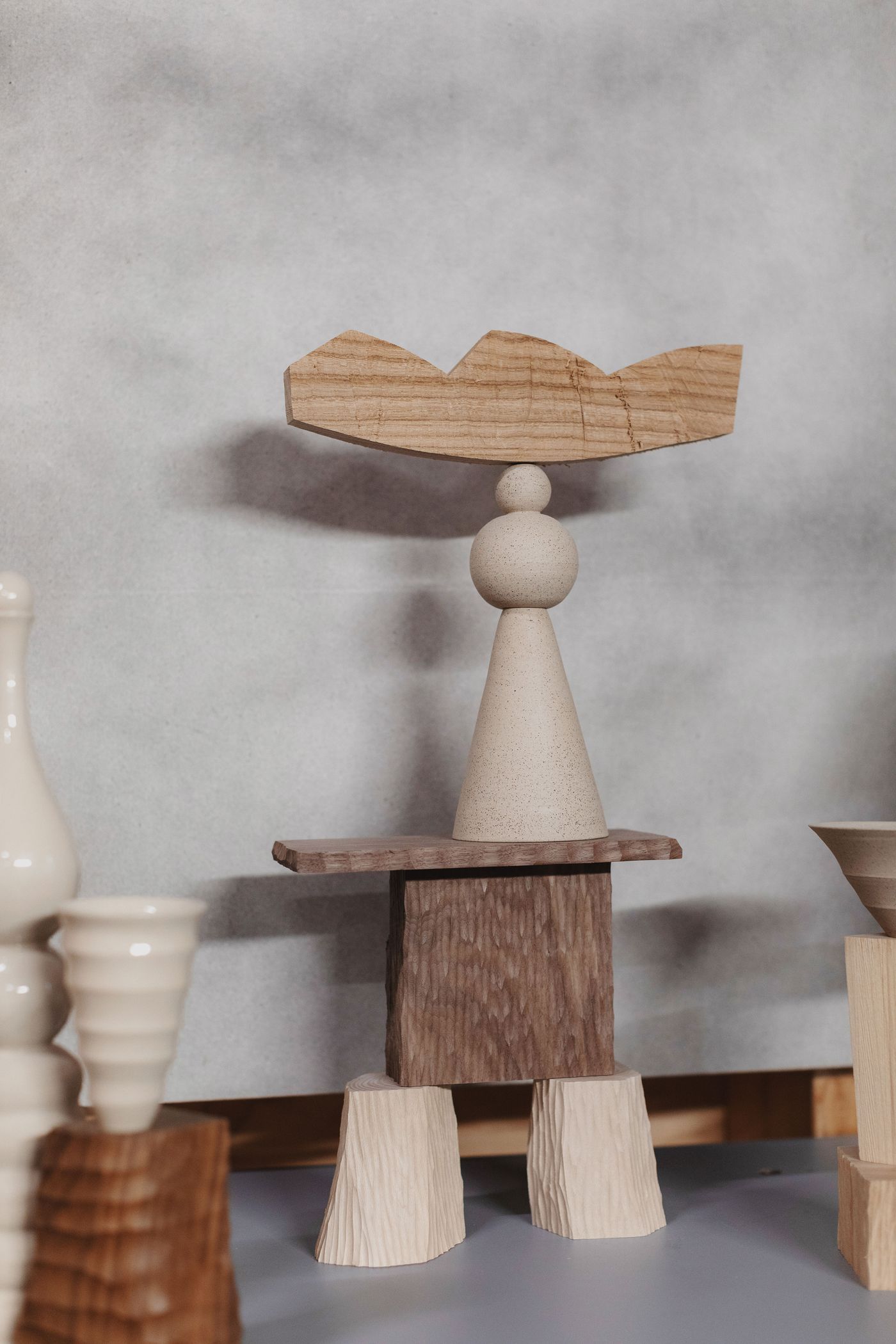 A composition of modern sculptures featuring wood and ceramic forms, including a tall cone topped with a flat wooden piece.