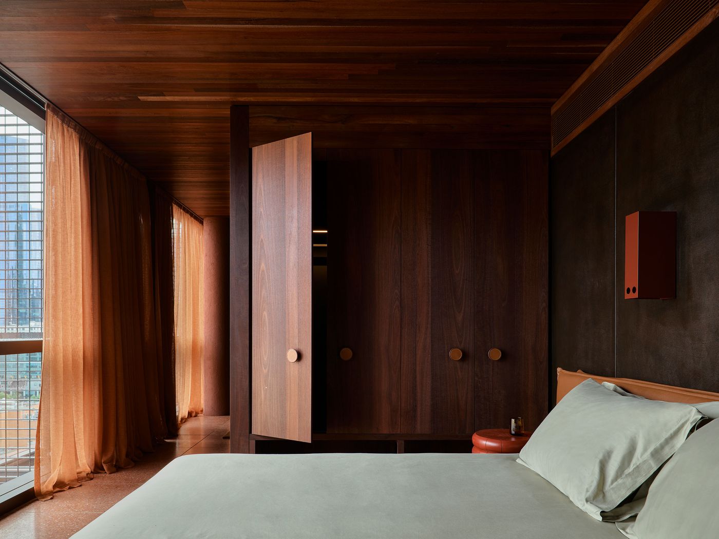 Stylish interior of a modern bedroom featuring wooden elements, orange curtains, and a neatly made bed with green linens. Stylish interior of a modern bedroom featuring wooden elements, orange curtains, and a neatly made bed with green linens.
