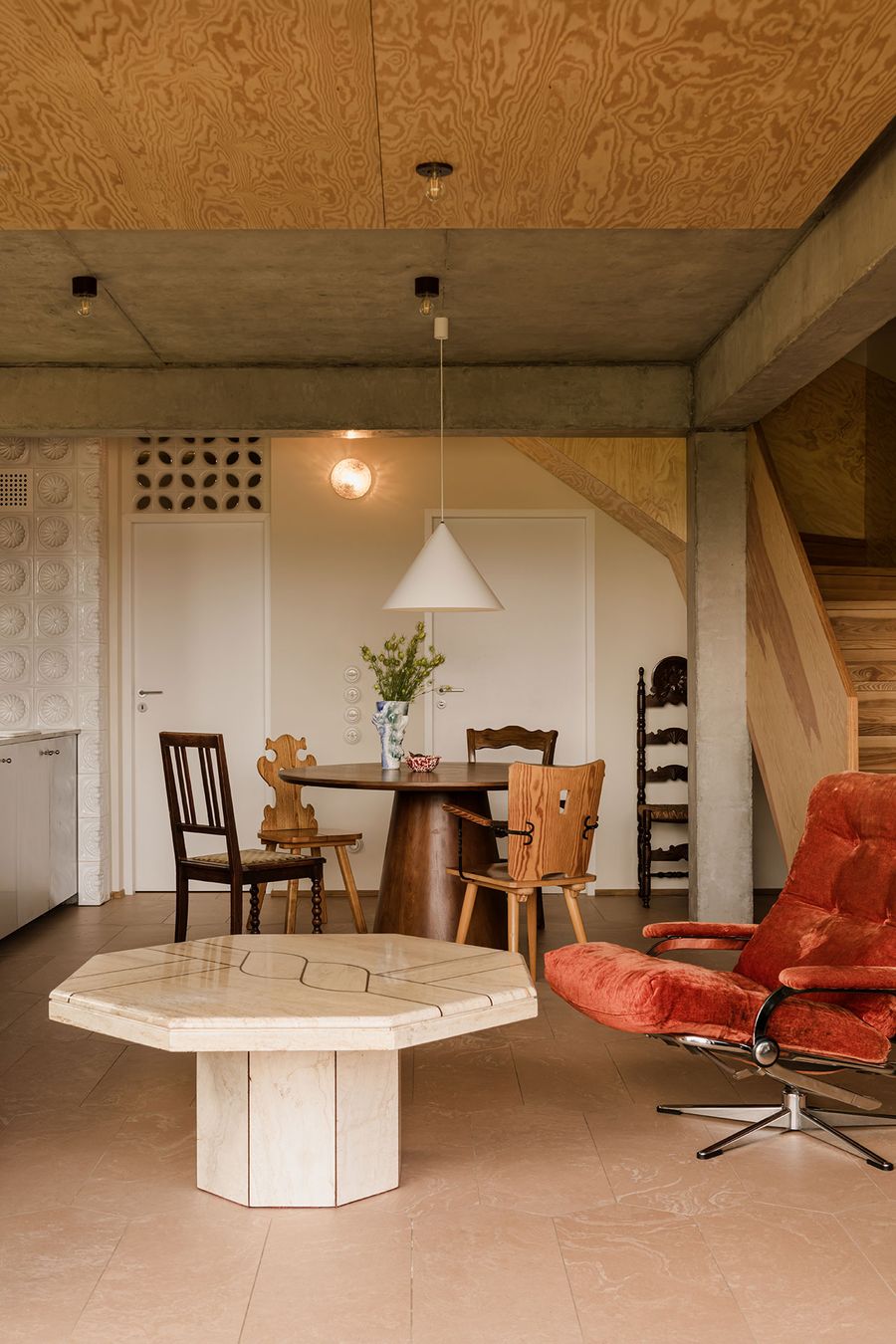Modern interior featuring a round wooden dining table, eclectic chairs, a marble coffee table, and a cozy orange recliner. Modern interior featuring a round wooden dining table, eclectic chairs, a marble coffee table, and a cozy orange recliner.