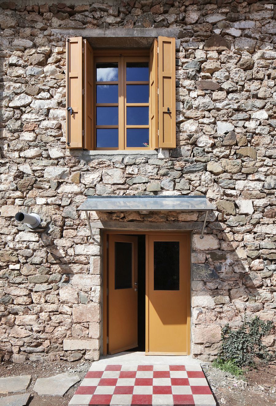 Warm honey-toned wooden shutters complement the natural limestone texture in this detail view. The traditional window treatment and robust stone masonry demonstrate authentic Mediterranean craftsmanship, where functional elements become expressive architectural features through material honesty.
