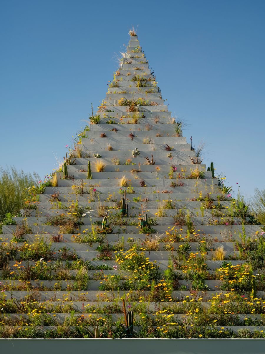 A stepped pyramid garden adorned with colorful flowers and cacti, set against a clear blue sky. A stepped pyramid garden adorned with colorful flowers and cacti, set against a clear blue sky.