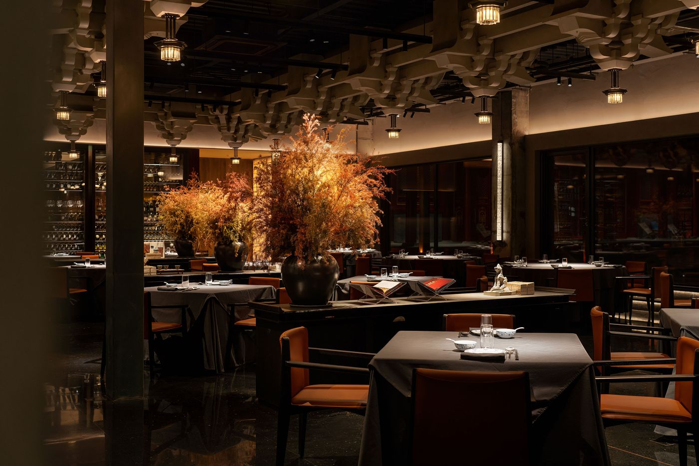 Elegant restaurant interior featuring ambient lighting, dark tables, and lush orange floral arrangements in large vases. Elegant restaurant interior featuring ambient lighting, dark tables, and lush orange floral arrangements in large vases.