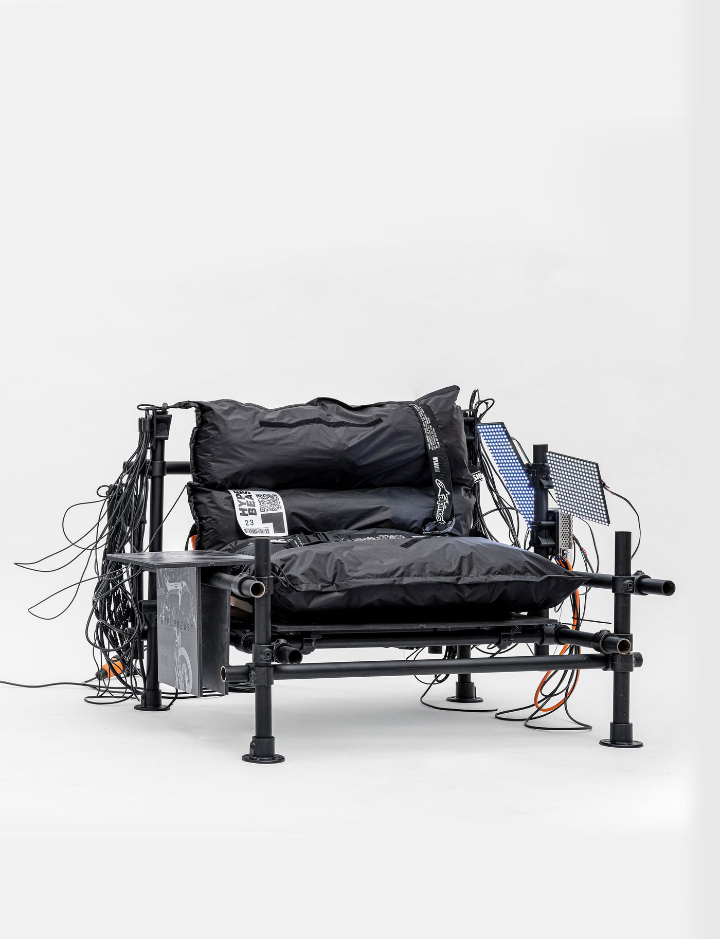 A contemporary black lounge chair with padded cushions, surrounded by tangled wires and connected devices. A contemporary black lounge chair with padded cushions, surrounded by tangled wires and connected devices.