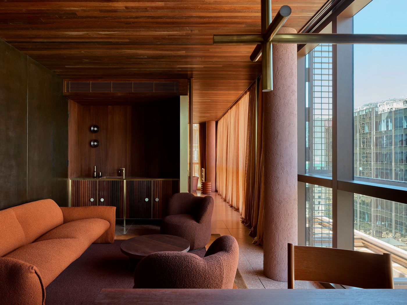 Modern interior with warm hues, featuring a textured orange sofa, round table, and large windows revealing a city skyline. Modern interior with warm hues, featuring a textured orange sofa, round table, and large windows revealing a city skyline.