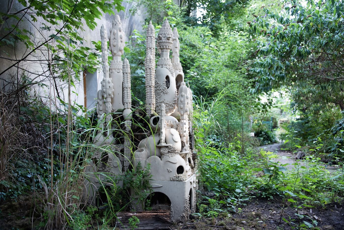 Overgrown sculpture of intricate towers and forms surrounded by lush green foliage in an abandoned area. Overgrown sculpture of intricate towers and forms surrounded by lush green foliage in an abandoned area.