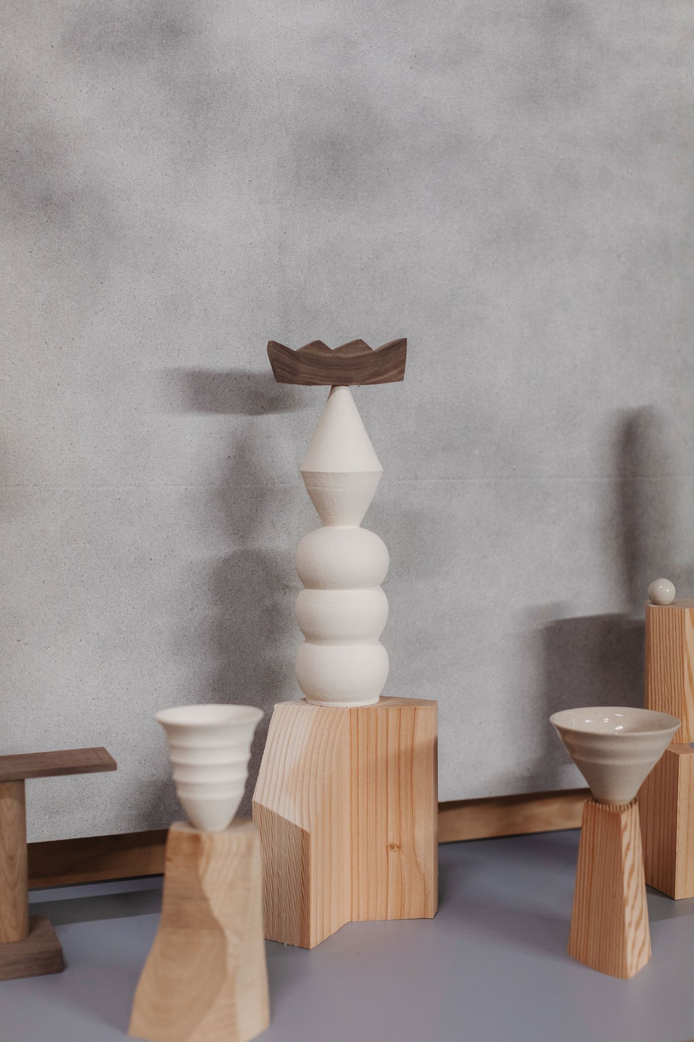 A composition of modern sculptures featuring wood and ceramic forms, including a tall cone topped with a flat wooden piece.