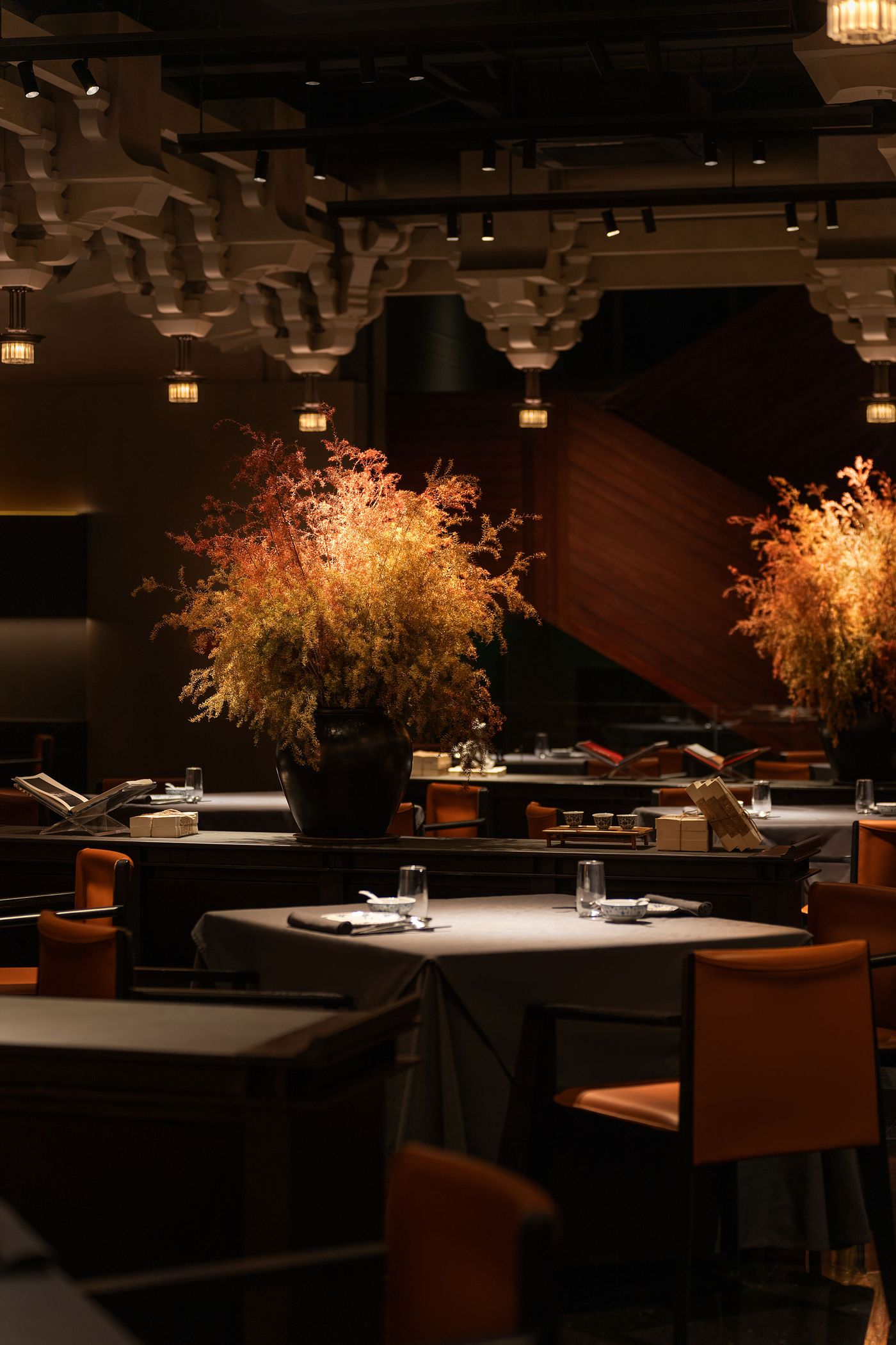 Elegant restaurant interior with dim lighting, featuring a large artistic floral centerpiece and well-set tables with orange chairs. Elegant restaurant interior with dim lighting, featuring a large artistic floral centerpiece and well-set tables with orange chairs.