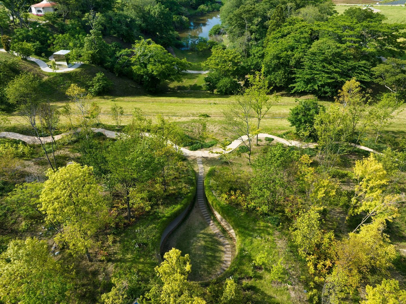 Aerial view of a lush green landscape with winding paths, trees, and a small pond, showcasing a tranquil, natural setting. Aerial view of a lush green landscape with winding paths, trees, and a small pond, showcasing a tranquil, natural setting.