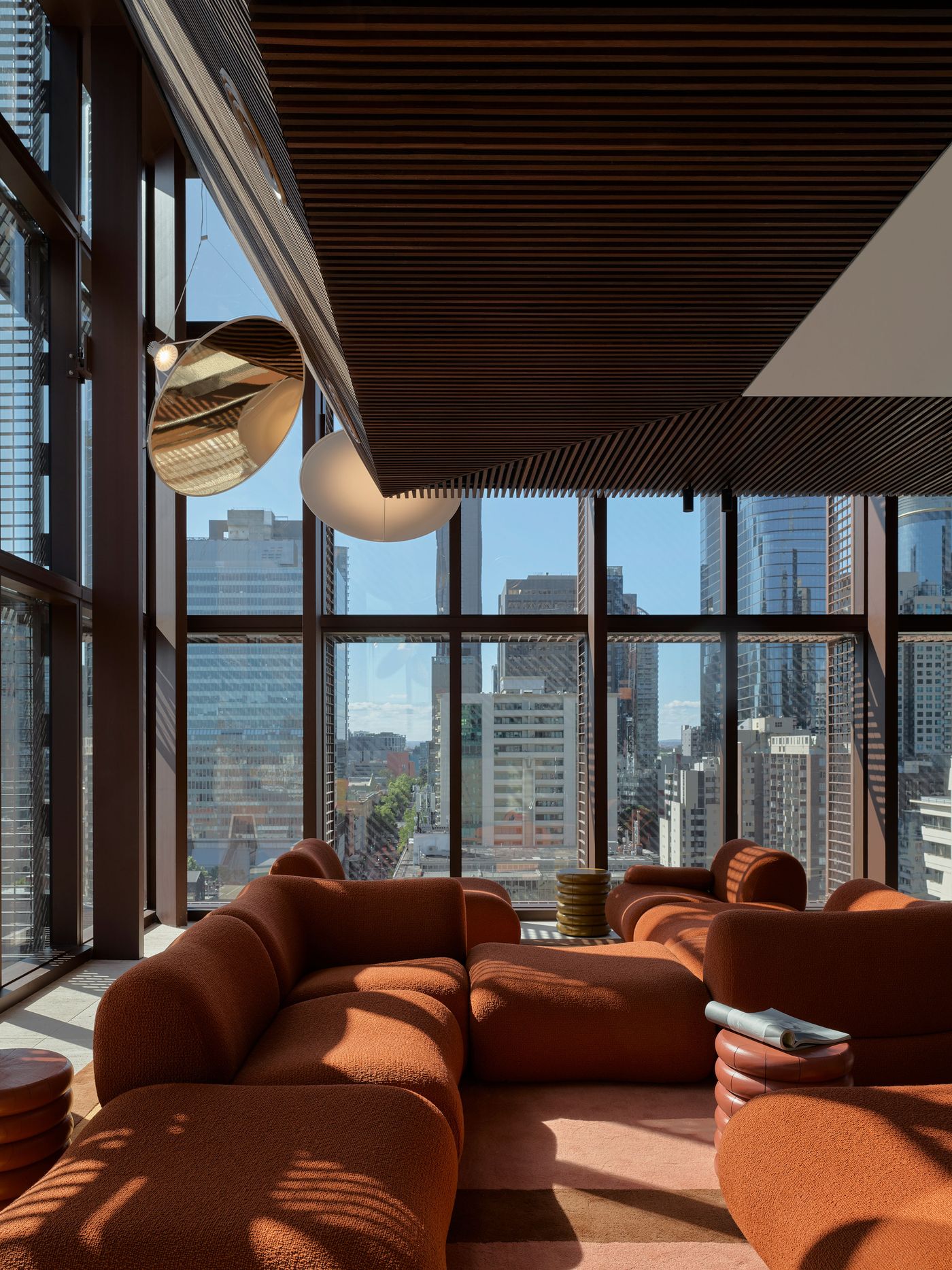 A modern lounge with an orange curved sofa, stylish decor, and large windows showcasing a vibrant city skyline under bright sunlight. A modern lounge with an orange curved sofa, stylish decor, and large windows showcasing a vibrant city skyline under bright sunlight.
