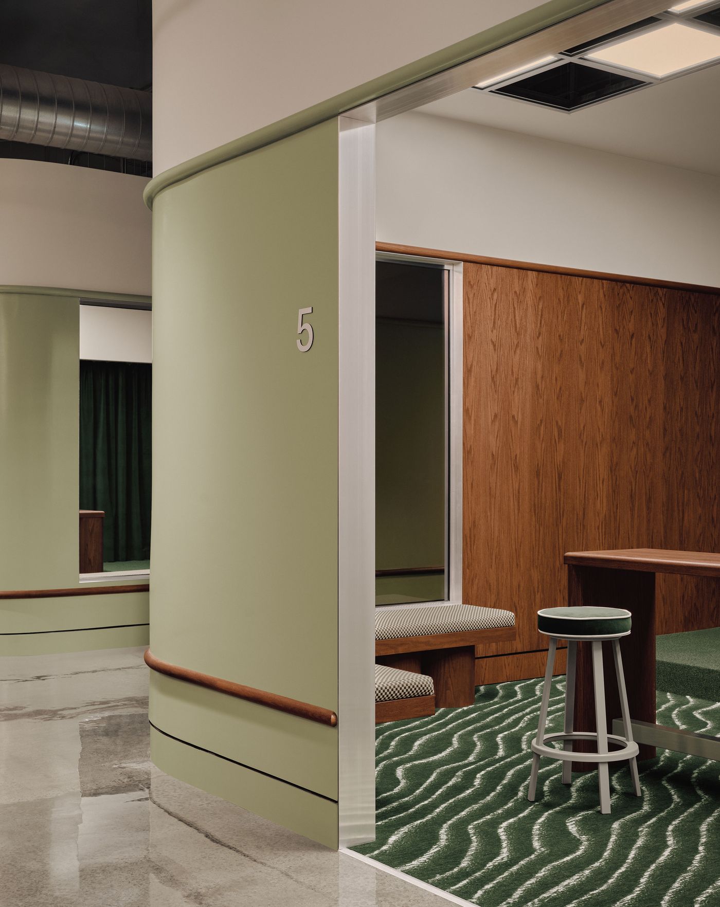 Modern interior featuring a green curved wall with the number 5, a cozy seating area, and a stylish stool on a textured rug.