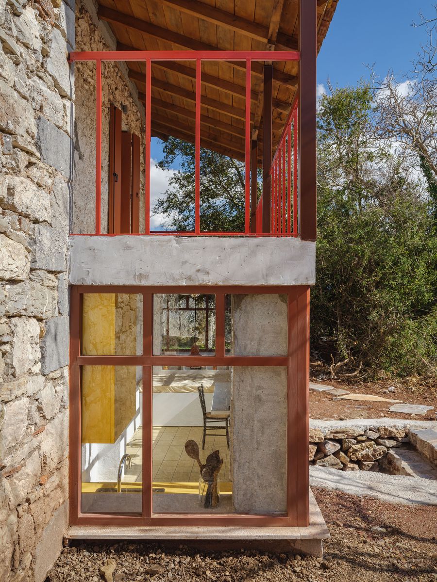 The coral-red steel addition cantilevers boldly from the historic stone wall, creating protected outdoor space. This architectural intervention demonstrates how contemporary elements can enhance traditional buildings while maintaining visual lightness and structural clarity in the landscape.