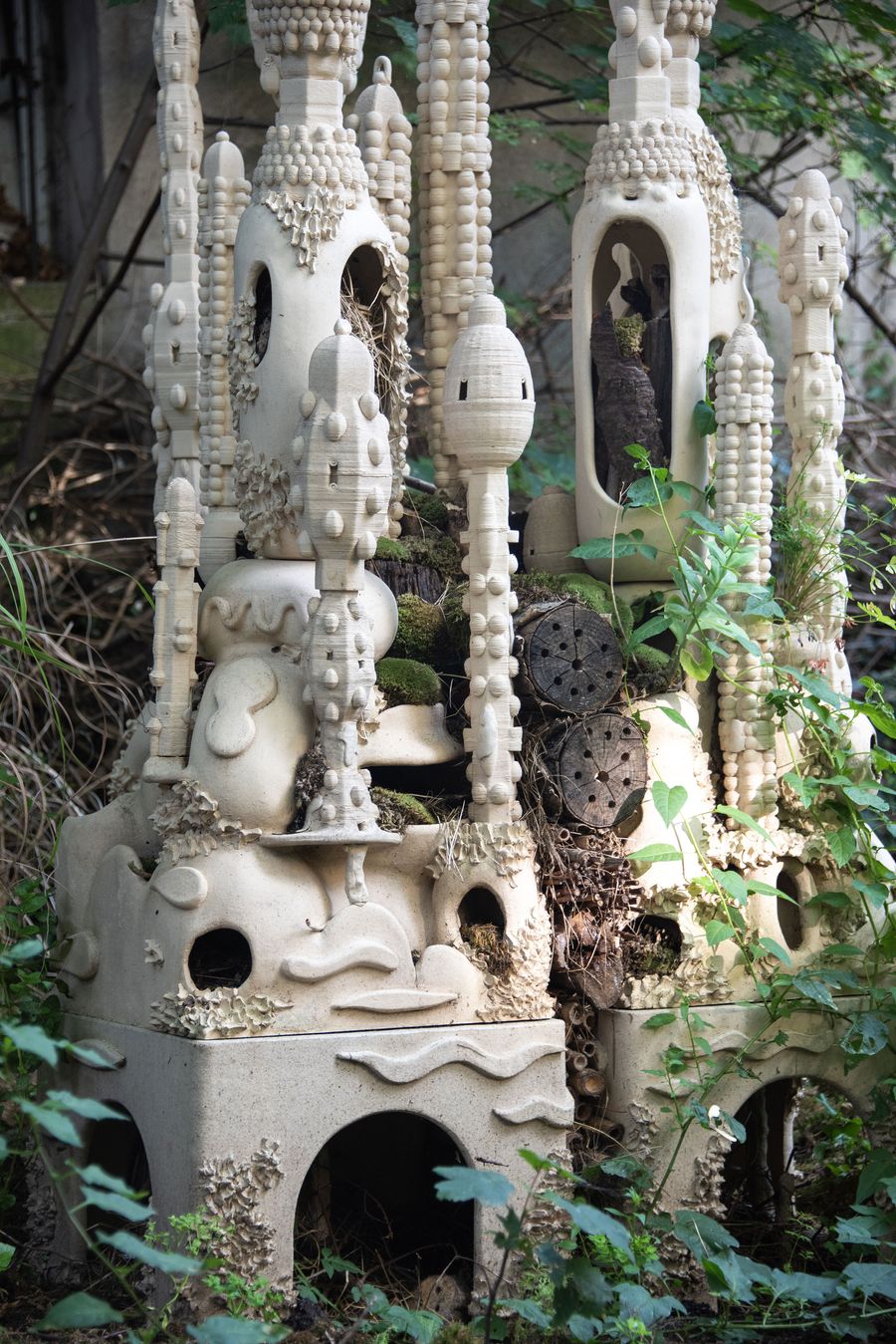 An intricate, sculptural structure resembling organic towers, covered in moss and surrounded by lush foliage, evokes a natural habitat. An intricate, sculptural structure resembling organic towers, covered in moss and surrounded by lush foliage, evokes a natural habitat.