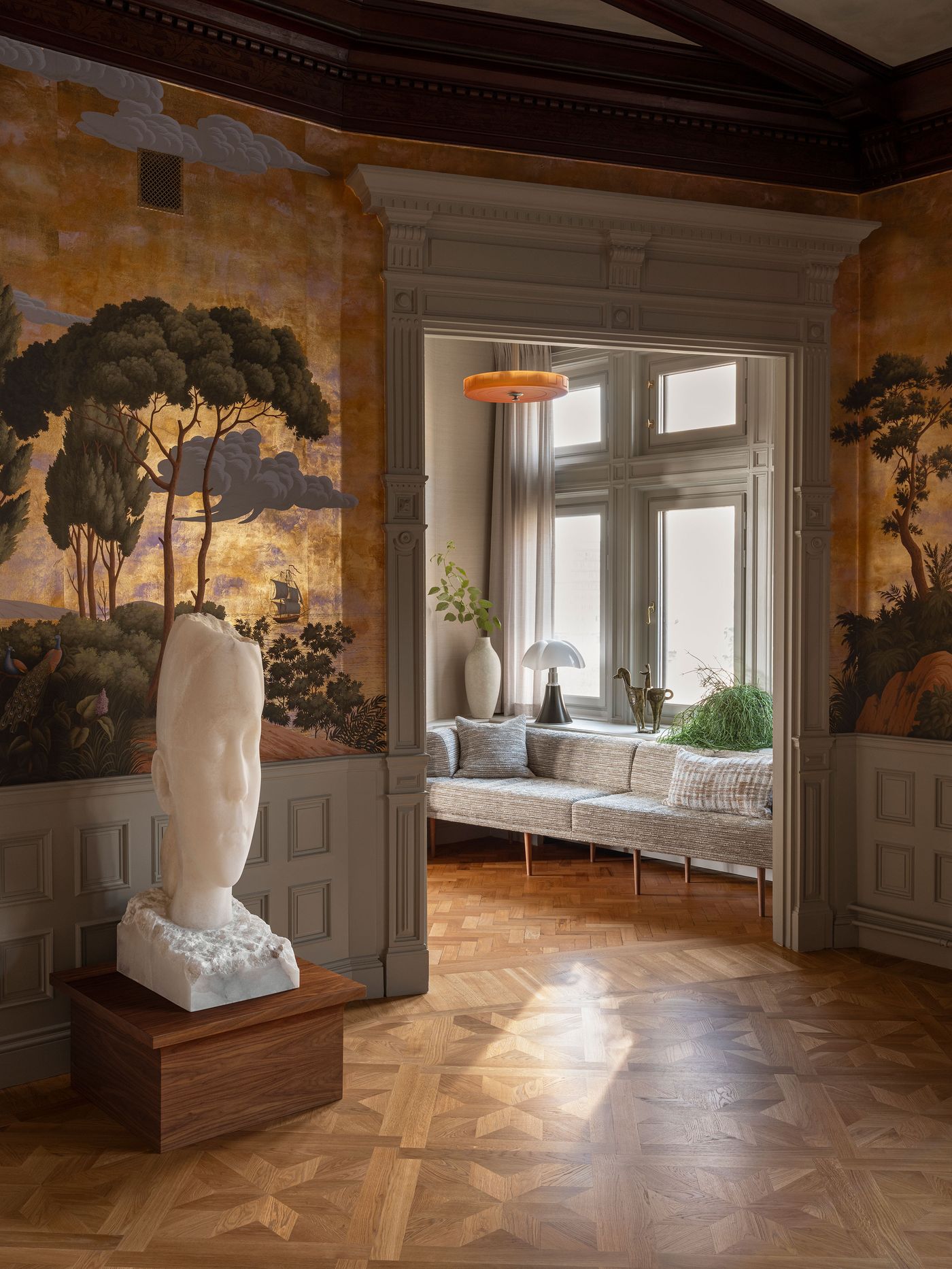 A stylish room featuring a marble head sculpture, vibrant mural, and modern furniture, illuminated by natural light and a pendant lamp. A stylish room featuring a marble head sculpture, vibrant mural, and modern furniture, illuminated by natural light and a pendant lamp.