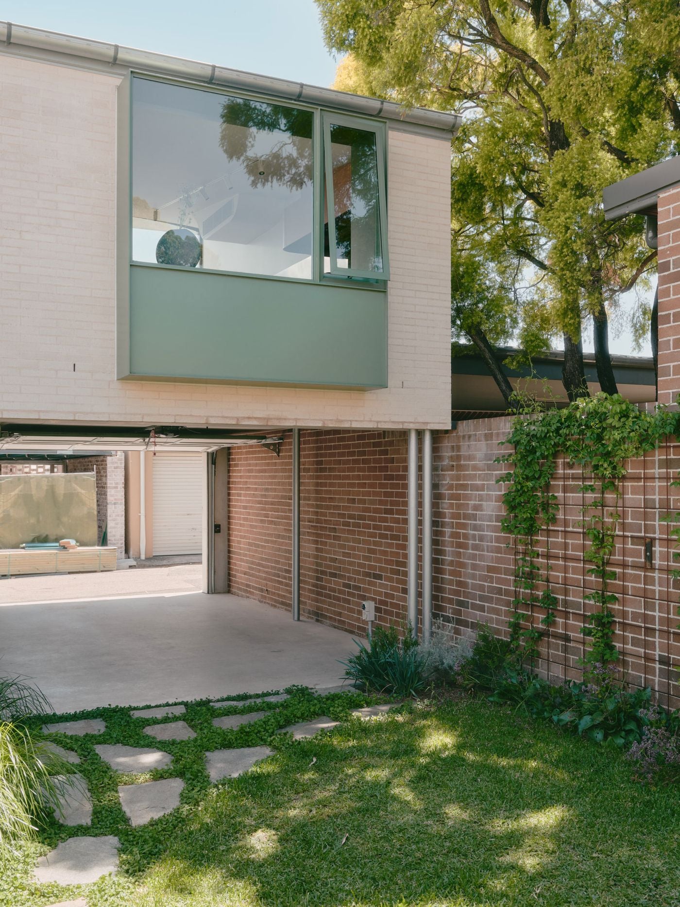 The garden-facing elevation shows the studio hovering above the fully open garage, conceived as a flexible covered room rather than solely vehicle storage. Pale brick, muted green framing and climbing plants create a restrained backdrop, while the open ground floor establishes a direct spatial connection through the property to the laneway. The garden-facing elevation shows the studio hovering above the fully open garage, conceived as a flexible covered room rather than solely vehicle storage. Pale brick, muted green framing and climbing plants create a restrained backdrop, while the open ground floor establishes a direct spatial connection through the property to the laneway.