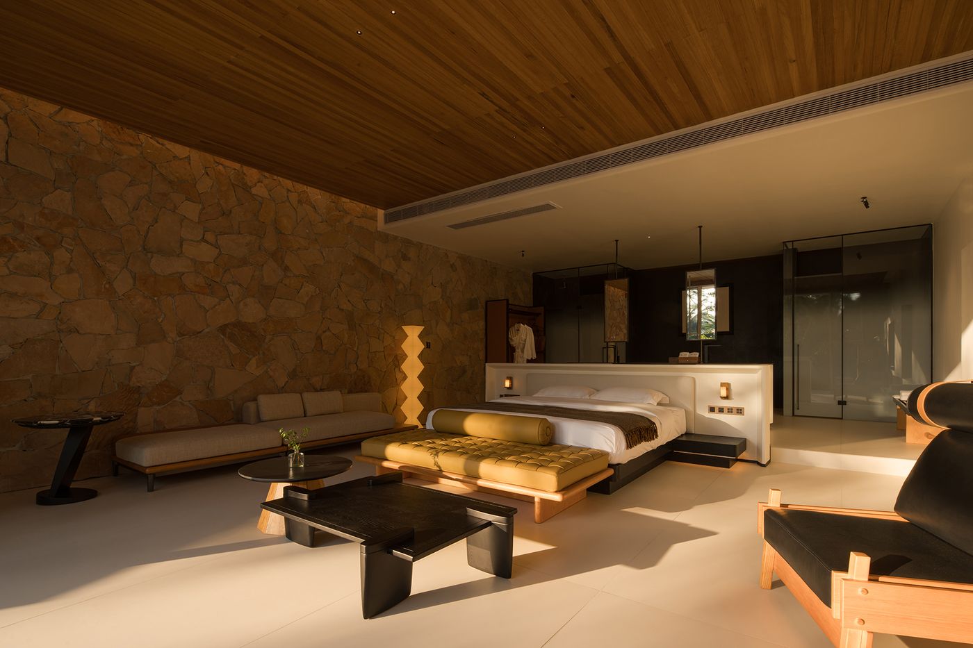 Modern, serene bedroom with stone wall, stylish furniture, and large windows allowing natural light to fill the space. Modern, serene bedroom with stone wall, stylish furniture, and large windows allowing natural light to fill the space.