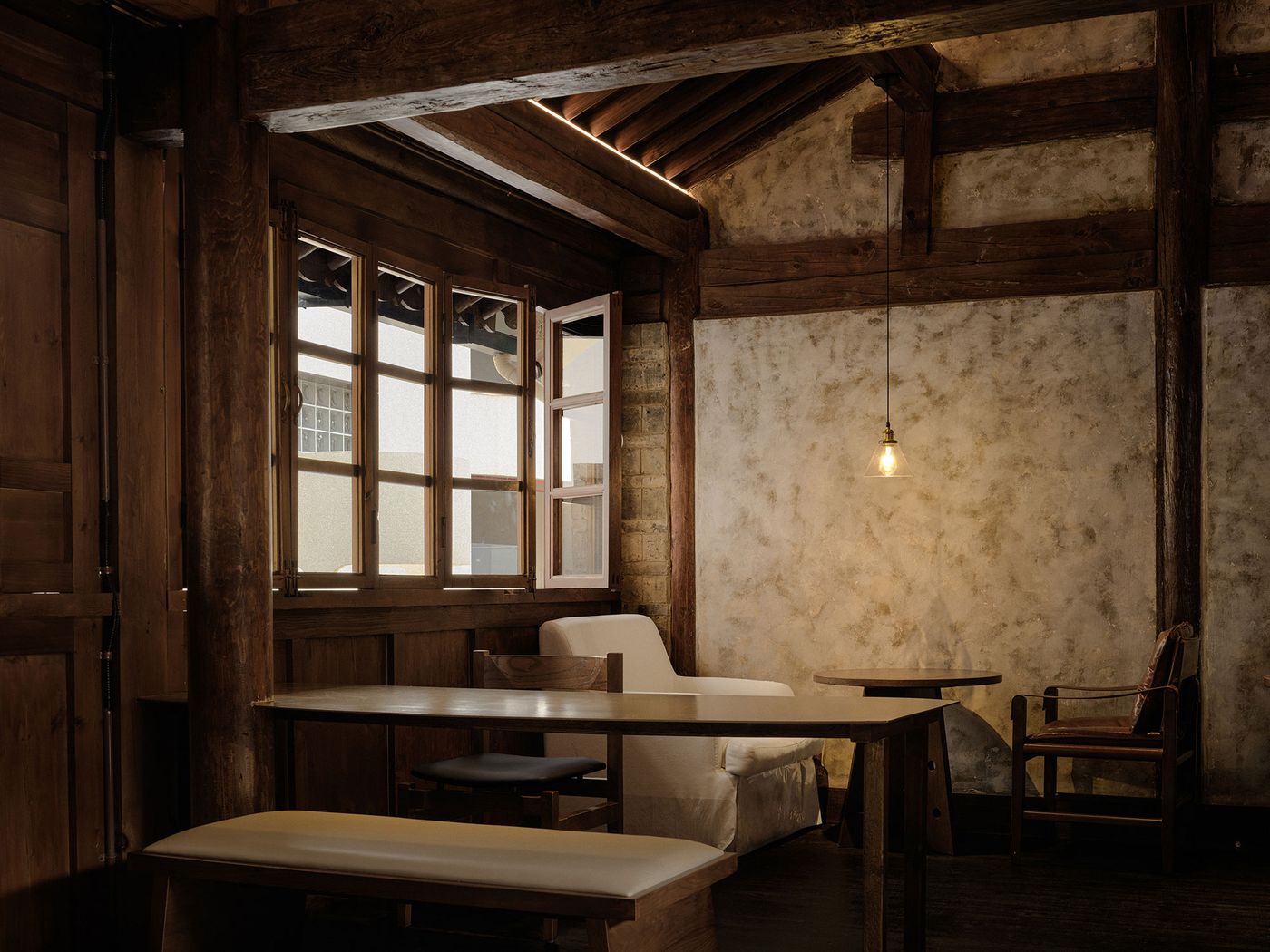 A cozy wooden room featuring large windows, a simple table with chairs, and a warm hanging light fixture illuminating the space. A cozy wooden room featuring large windows, a simple table with chairs, and a warm hanging light fixture illuminating the space.