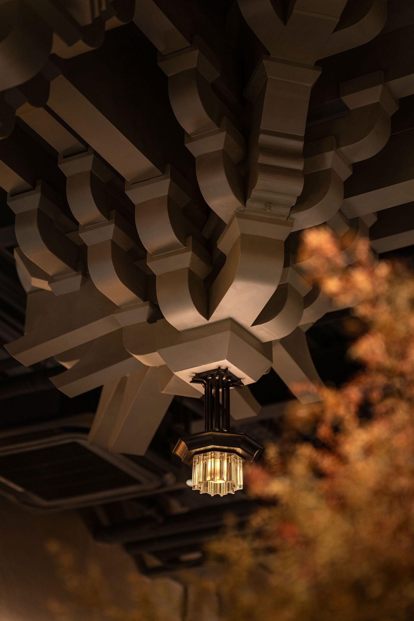 An ornate ceiling design featuring sculpted beams and a vintage-style chandelier, softly illuminated against a blurred background. An ornate ceiling design featuring sculpted beams and a vintage-style chandelier, softly illuminated against a blurred background.