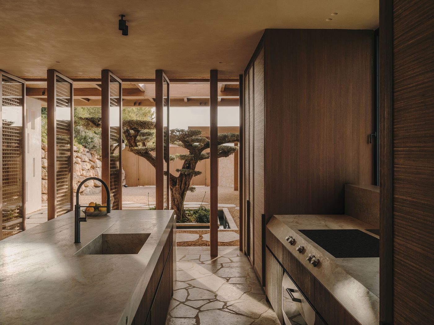Modern kitchen with stone countertops, sleek appliances, and large glass doors overlooking a serene outdoor garden with a bonsai tree. Modern kitchen with stone countertops, sleek appliances, and large glass doors overlooking a serene outdoor garden with a bonsai tree.