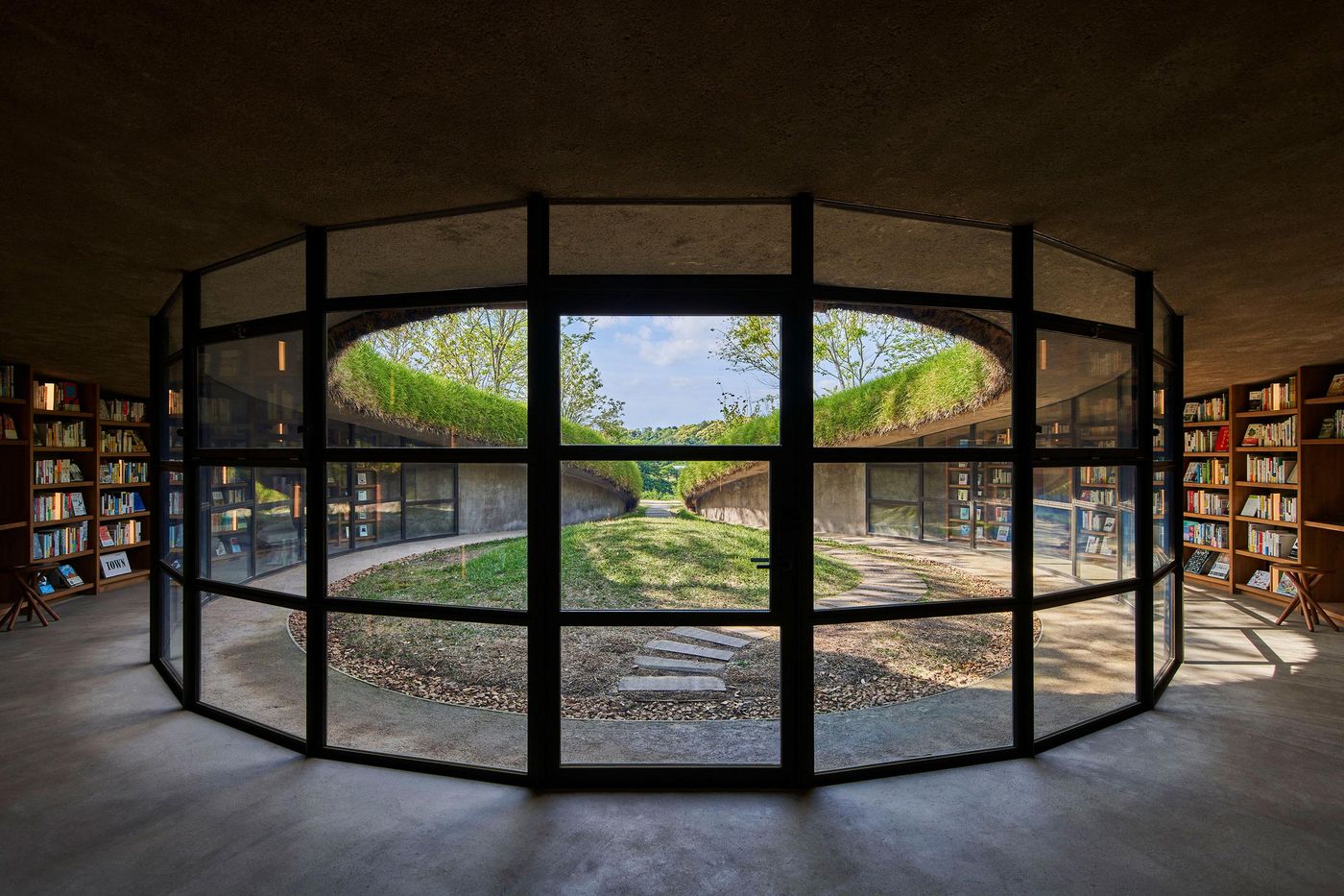 A modern library with large glass windows, showcasing a green courtyard and shelves lined with books inside. A modern library with large glass windows, showcasing a green courtyard and shelves lined with books inside.