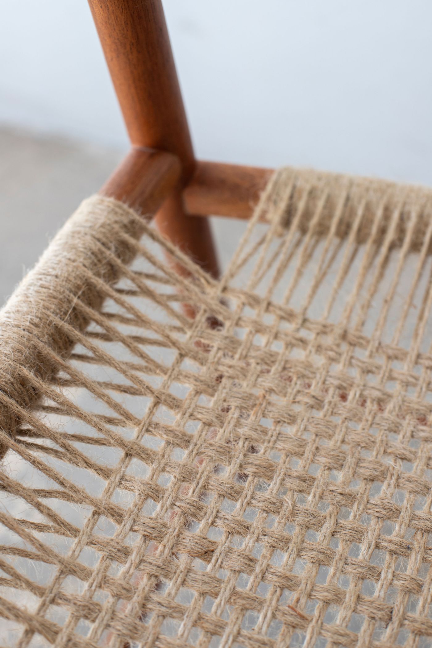 A close-up reveals the intricate weave of natural fiber basketry, showcasing traditional craftsmanship where golden jute strands intersect in geometric patterns. The warm wooden handle contrasts against the organic texture, emphasizing the tactile quality of artisanal rope work and sustainable materials in contemporary design.