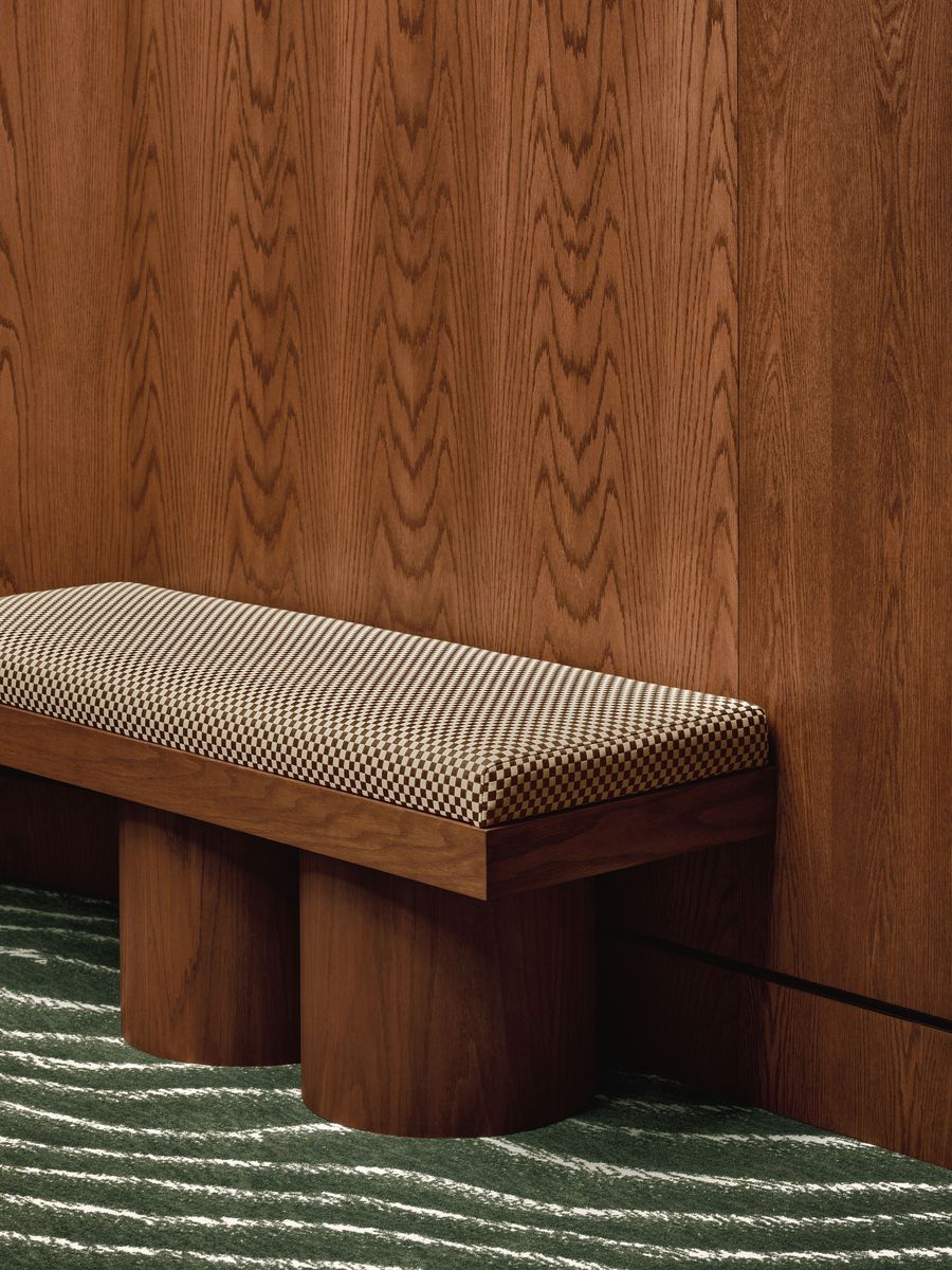 A modern bench with a checkered cushion sits against a rich wooden wall, complemented by a green wavy patterned carpet. A modern bench with a checkered cushion sits against a rich wooden wall, complemented by a green wavy patterned carpet.