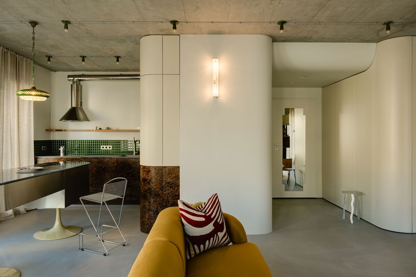 A wide shot reveals the apartment’s cohesive palette and modular layout, where soft curves, industrial ceilings, and refined finishes converge. The sculptural island, midcentury seating, and punctuating art pieces echo Mistovia’s vision of functional artistry with a retro-futurist soul. A wide shot reveals the apartment’s cohesive palette and modular layout, where soft curves, industrial ceilings, and refined finishes converge. The sculptural island, midcentury seating, and punctuating art pieces echo Mistovia’s vision of functional artistry with a retro-futurist soul.