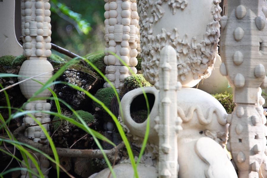 A close-up of artistic ceramic sculptures with varied textures, surrounded by moss and greenery, creating a natural, whimsical atmosphere.
